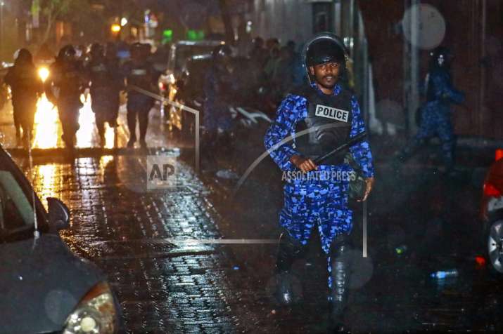 A Maldives policeman charges with baton towards protesters