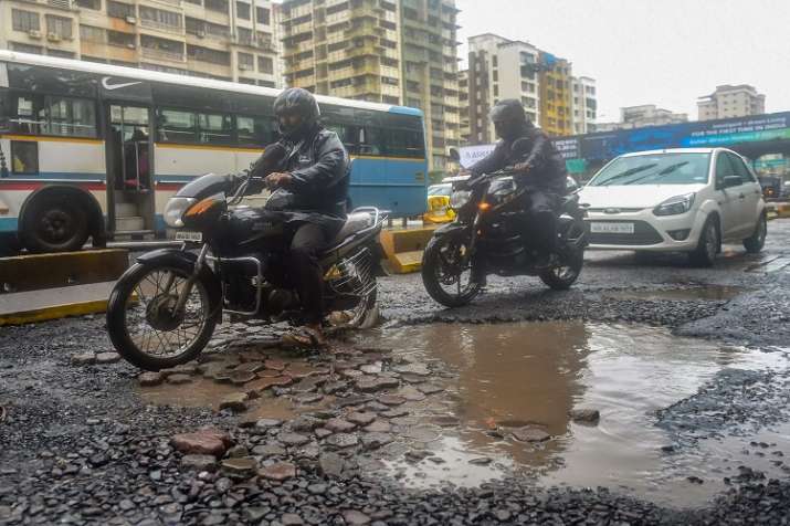 Commuters ride past pot-holes filled road after heavy