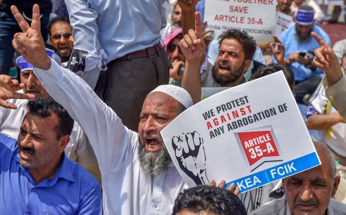 India Tv - Srinagar: Kashmiri traders hold placards and raise slogans during a sit-in protest against the petitions in the Supreme Court challenging the validity of Article 35A, in Srinagar on Sunday, August 05, 2018.