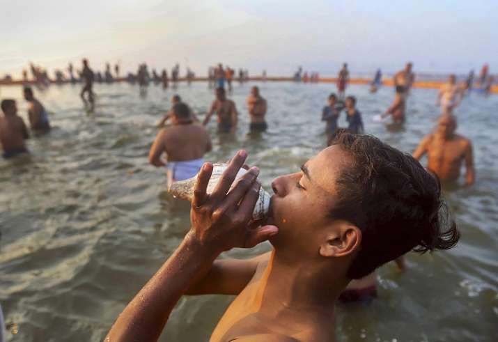 A devotee blows a conch shell after taking a holy dip at