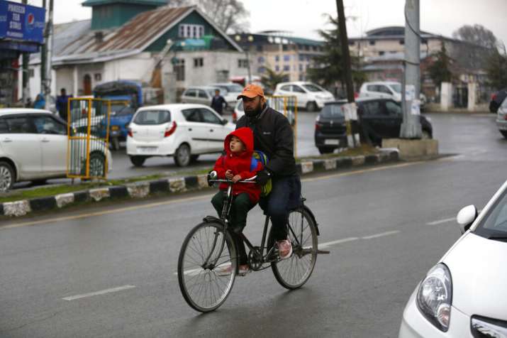 India Tv - A Kashmiri man carries a boy to school on a bicycle in Srinagar, Monday, March 11, 2019. Schools in Indian Kashmir reopened Monday after a three months winter break. (AP Photo)