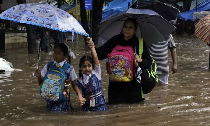 India Tv - Girls and their mother wade through a flooded street in Mumbai.
