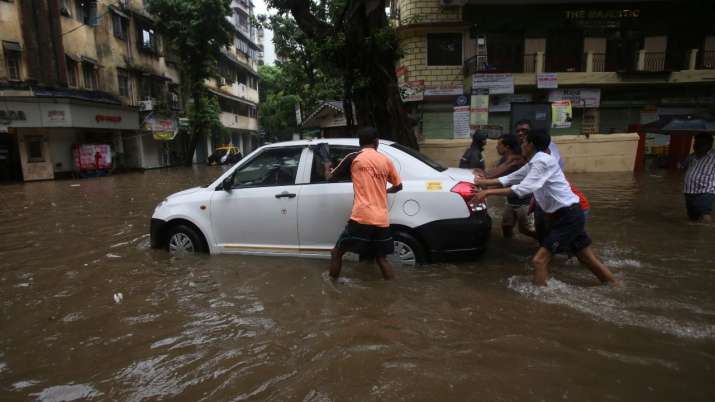 India Tv - People push a car through the flooded roads of Mumbai as it wade through a waterlogged street following heavy monsoon rain.
