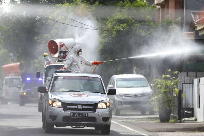 India Tv - Members of Indonesian Red Cross stand on the back of a truck and spray disinfectant in an attempt to