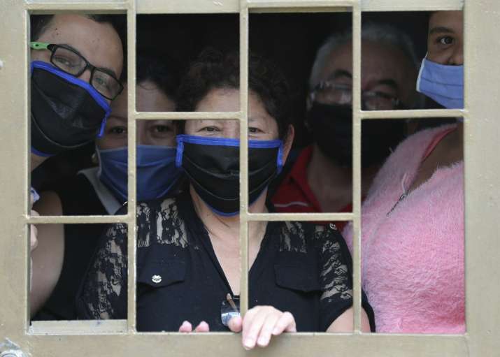 A family peers from the window of their home as they wait to receive boxes of free food, during a lo