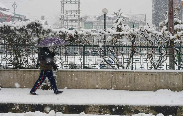 India Tv - Srinagar: A pedestrian holding an umbrella walks on a snow-covered pavement during snowfall in Srinagar, Sunday, Jan. 3, 2021. 