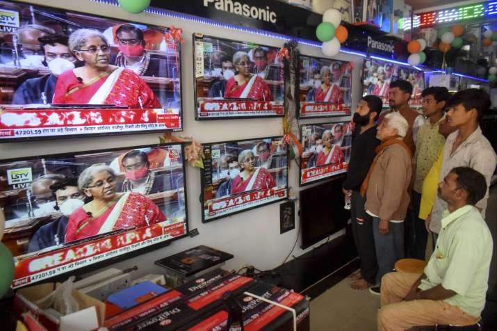 India Tv - People watch Finance Minister Nirmala Sitharaman presenting Union Budget 2021-21 on television sets, at an electronics store in Prayagraj, Monday, Feb. 01, 2021.