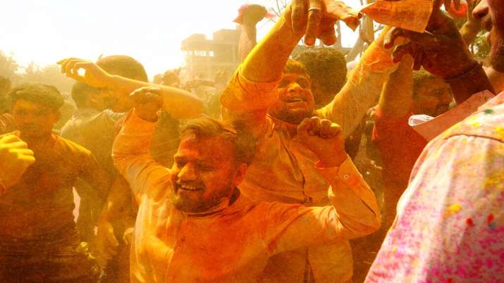Hindu devotees dance as colored powder is thrown on them at