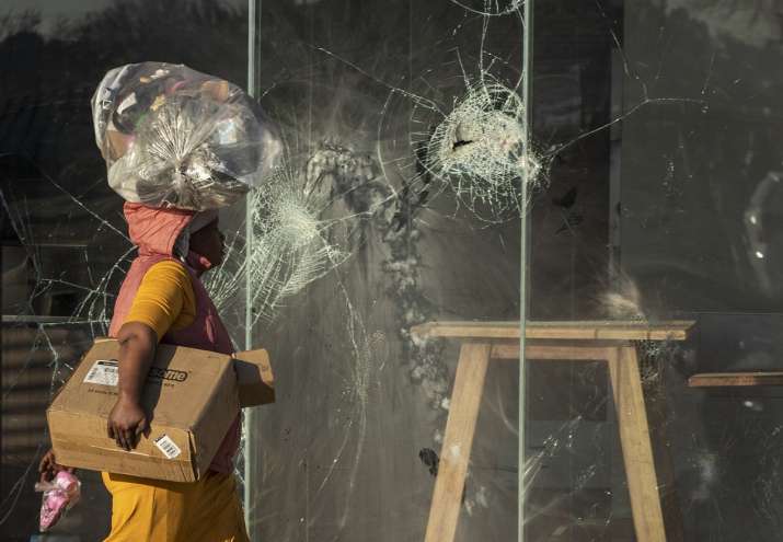 India Tv - A woman carrying groceries on her head walks past a damaged KFC fast food restaurant at the Naledi shopping complex in Vosluras, east of Johannesburg, South Africa.