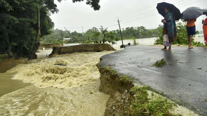 India Tv - Locals watch a stretch of road washed away by flood waters at Dhammadhama in Nalbari district of Assam