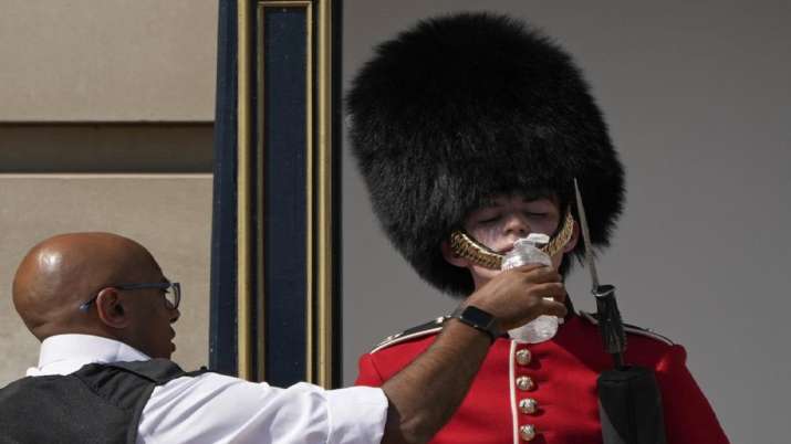 India Tv - A police officer gives water to a British soldier wearing the traditional bear hat on guard duty outside Buckingham Palace during warm weather in London. 