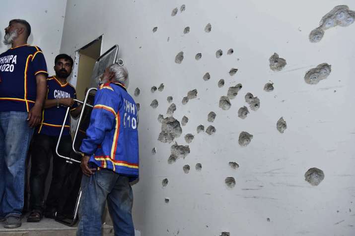 India Tv - Rescue workers stand beside a bullet-riddled wall after security forces conducting operation against attackers at a police headquarters, in Karachi.