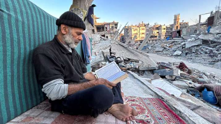 India Tv - Palestinian man Ismail Al-Khlout reads the Koran as he waits to break his fast while sitting on the 