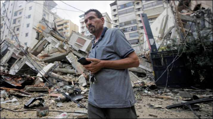 इंडिया टीवी - बेरूत के दक्षिणी उपनगरों पर इजरायली हमलों के बाद क्षतिग्रस्त इमारतों के पास एक व्यक्ति खड़ा है।