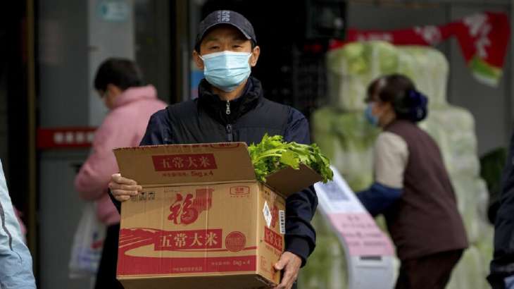 Seorang pria yang memakai masker wajah membawa sebuah kotak berisi bahan makanan