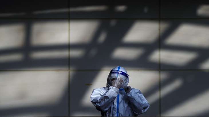 A worker in protective suit wipes his face shield at a