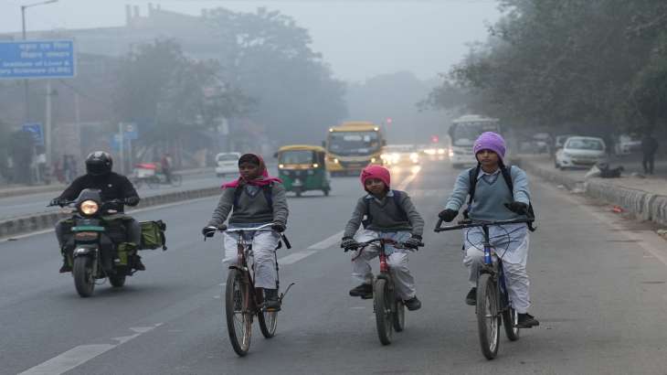 School children ride cycles to their school during a cold