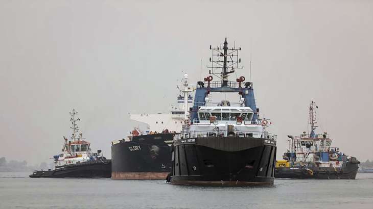 Tugboats pull a ship in the Suez Canal between the cities