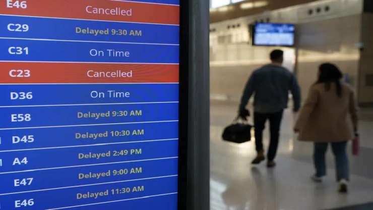 Travelers walk as a video board shows flight delays and cancellations at Ronald Reagan Washington National Airport in Arlington - India Tv